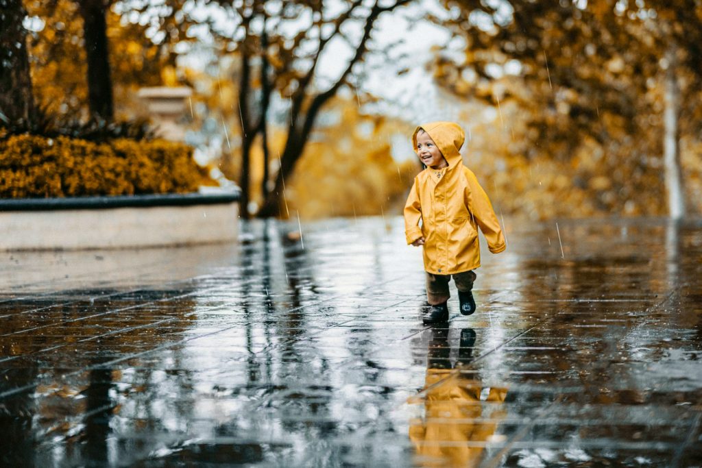 child in brown coat standing on water during daytime
